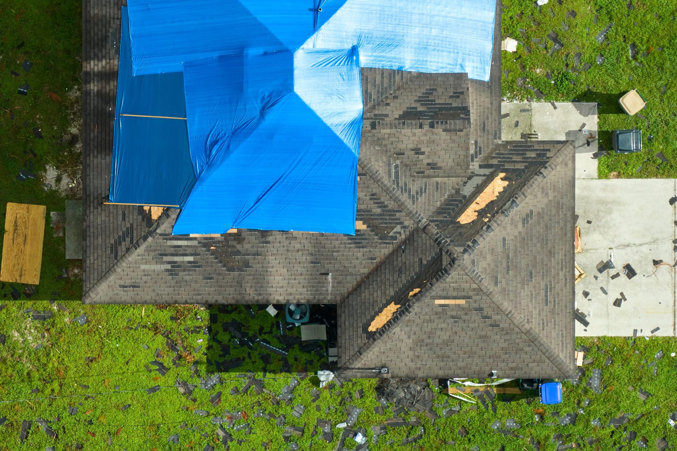 Top view of leaking house roof covered with protective tarp sheets against rain water leaks until replacement of asphalt shingles. Damage of building rooftop as aftermath