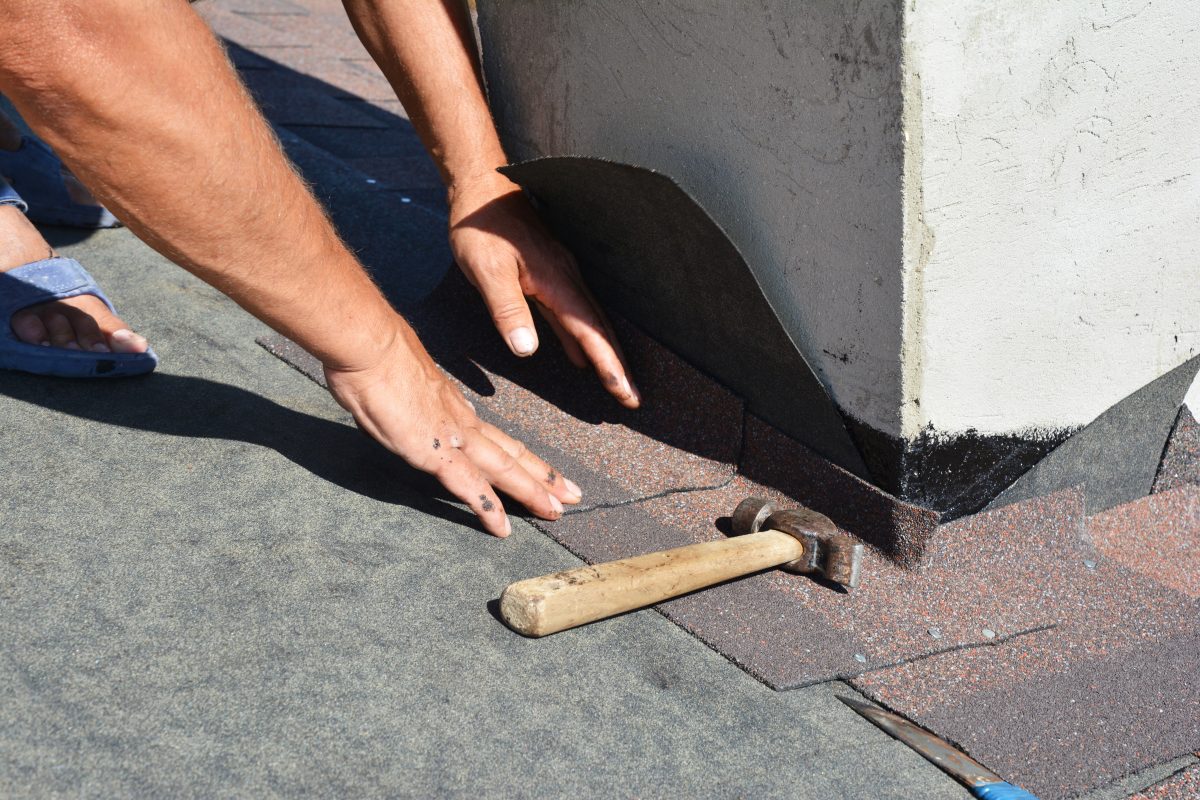 hail damage signs Asphalt shingles roofing construction. Roofer repair and laying asphalt shingles with vapor barrier in chimney problem area. Chimney waterproofing on house rooftop.